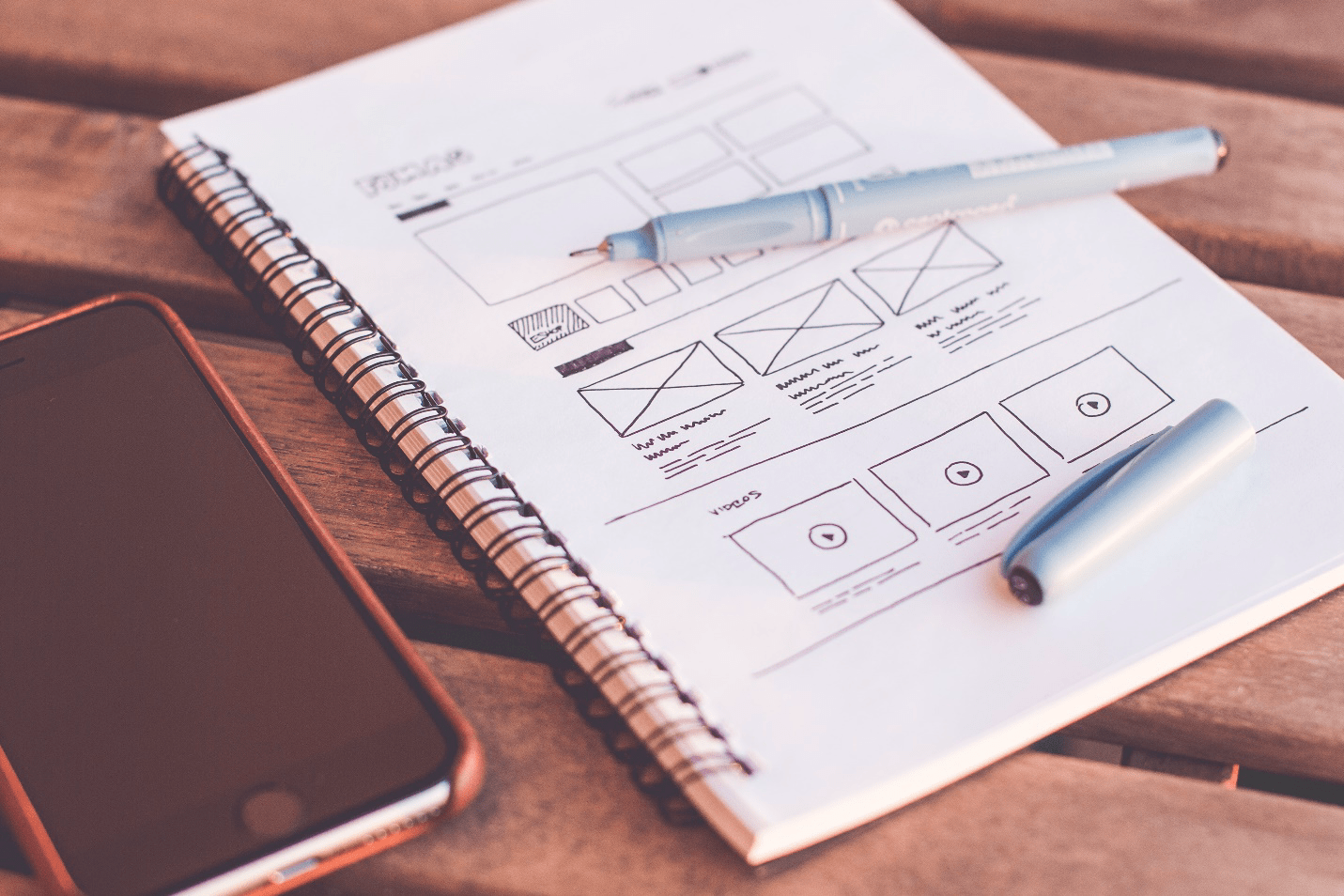 A notebook with a sketch of rectangles and icons lies open with a pen on top