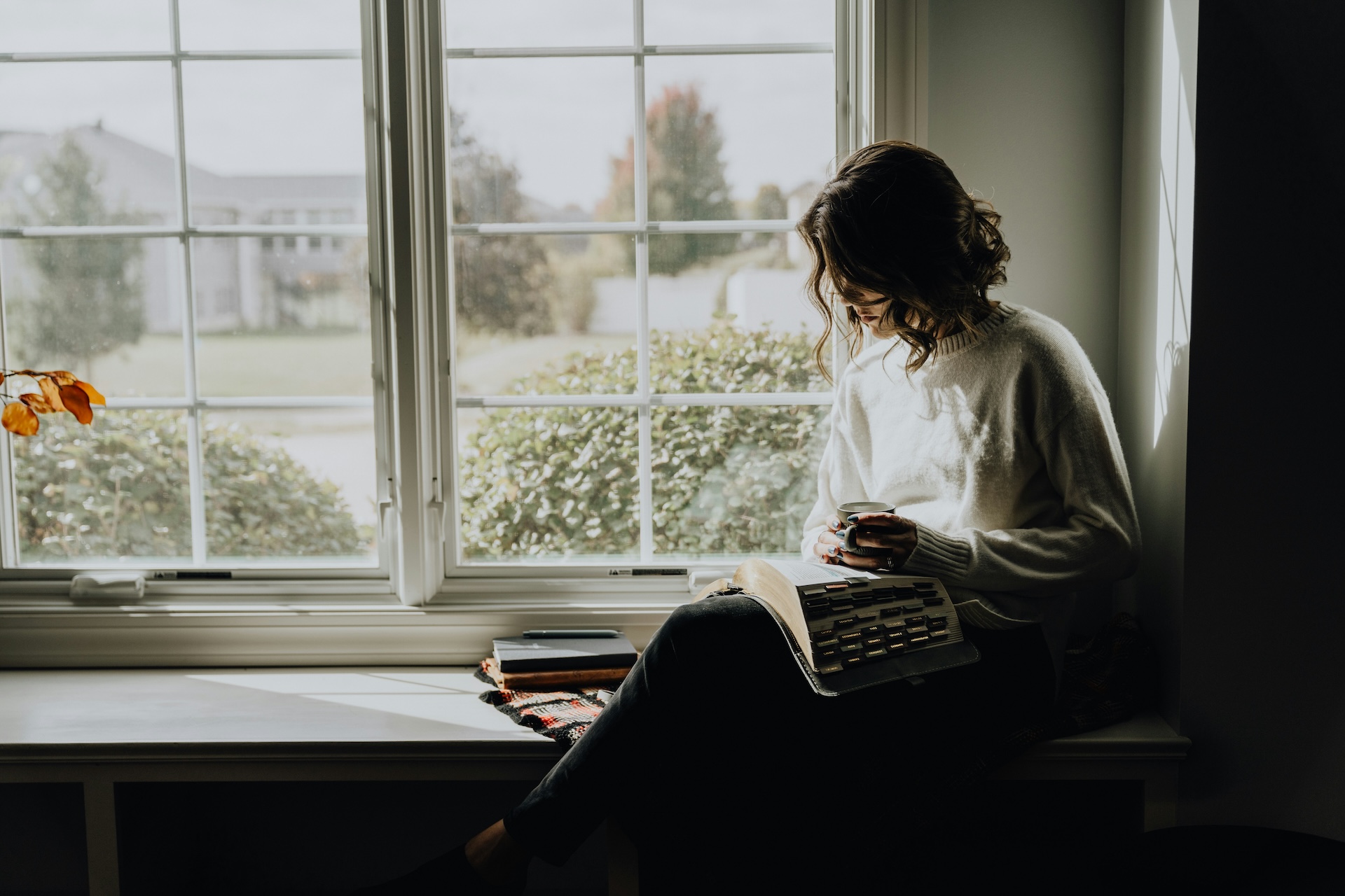a woman sitting on a window sill reading a book